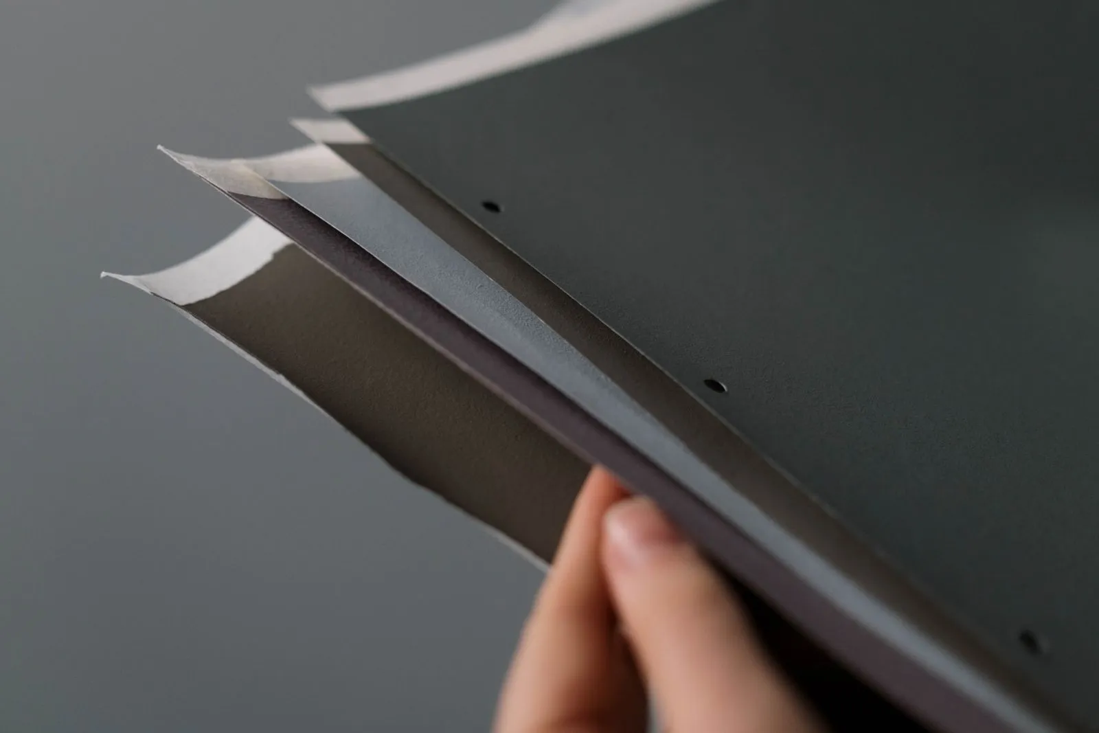 A close-up of a hand holding a set of gray paper samples against a neutral background.